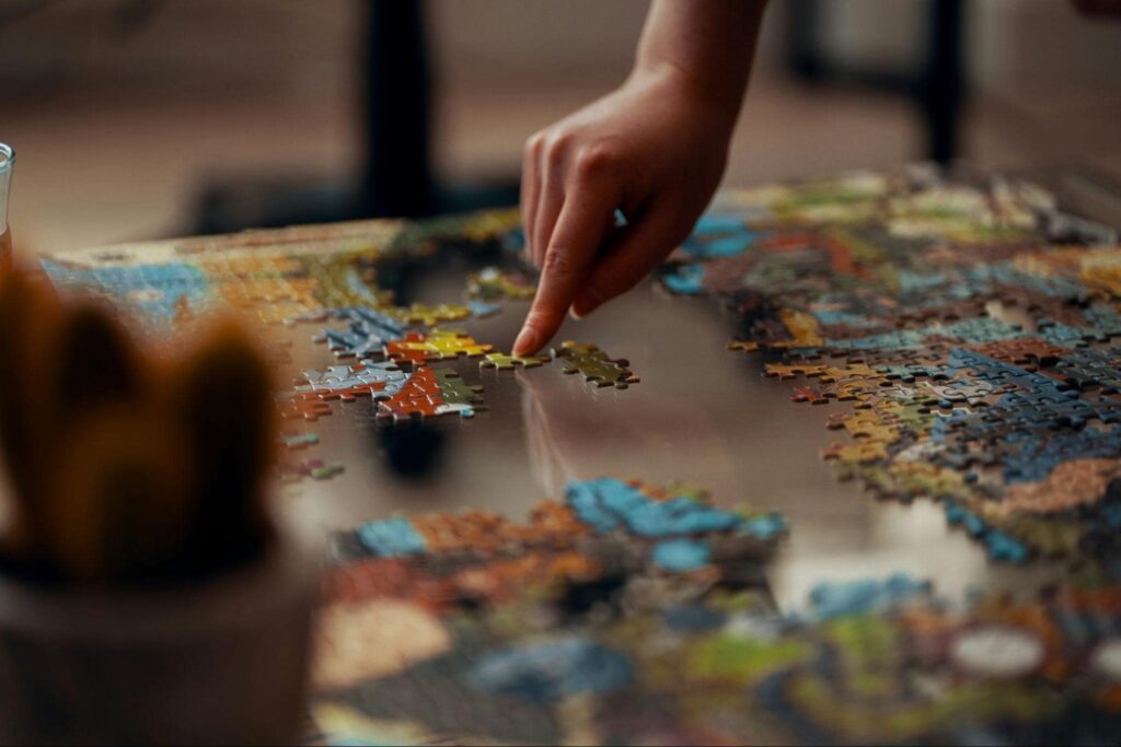 A hand moving puzzle pieces on a glass table.