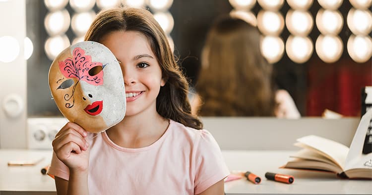 A girl with a type of character-painted mask sitting in front of a desk with a mirror.