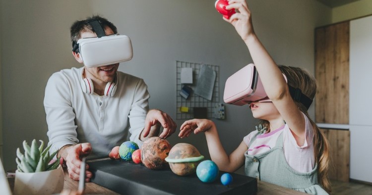 A little girl and her dad, both wearing VR headsets as they use a model of the solar system.