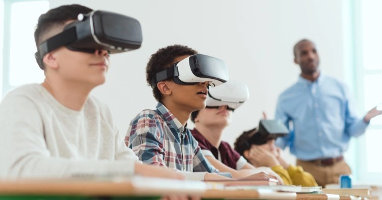 Four boys wearing VR headsets in class while their teacher instructs them.