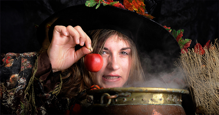 A woman wearing a witch hat and robe while holding a red apple, displaying what makes a good villain