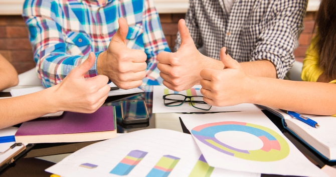 A group of children with their thumbs up over their statistics notes, which are on a table.