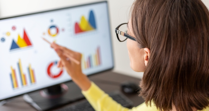 A woman with glasses using a stylus to study learning analytics on a desktop monitor.