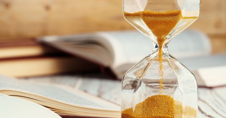 A number of open books next to an hourglass with falling sand as a metaphor for how to end a story