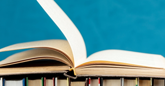 An open book set on a group of vertical books, all against a teal background.