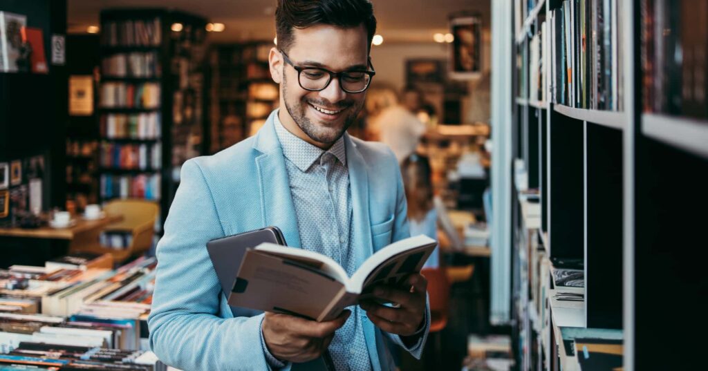 A man with glasses is absorbed in a book, surrounded by the tranquil atmosphere of a library.